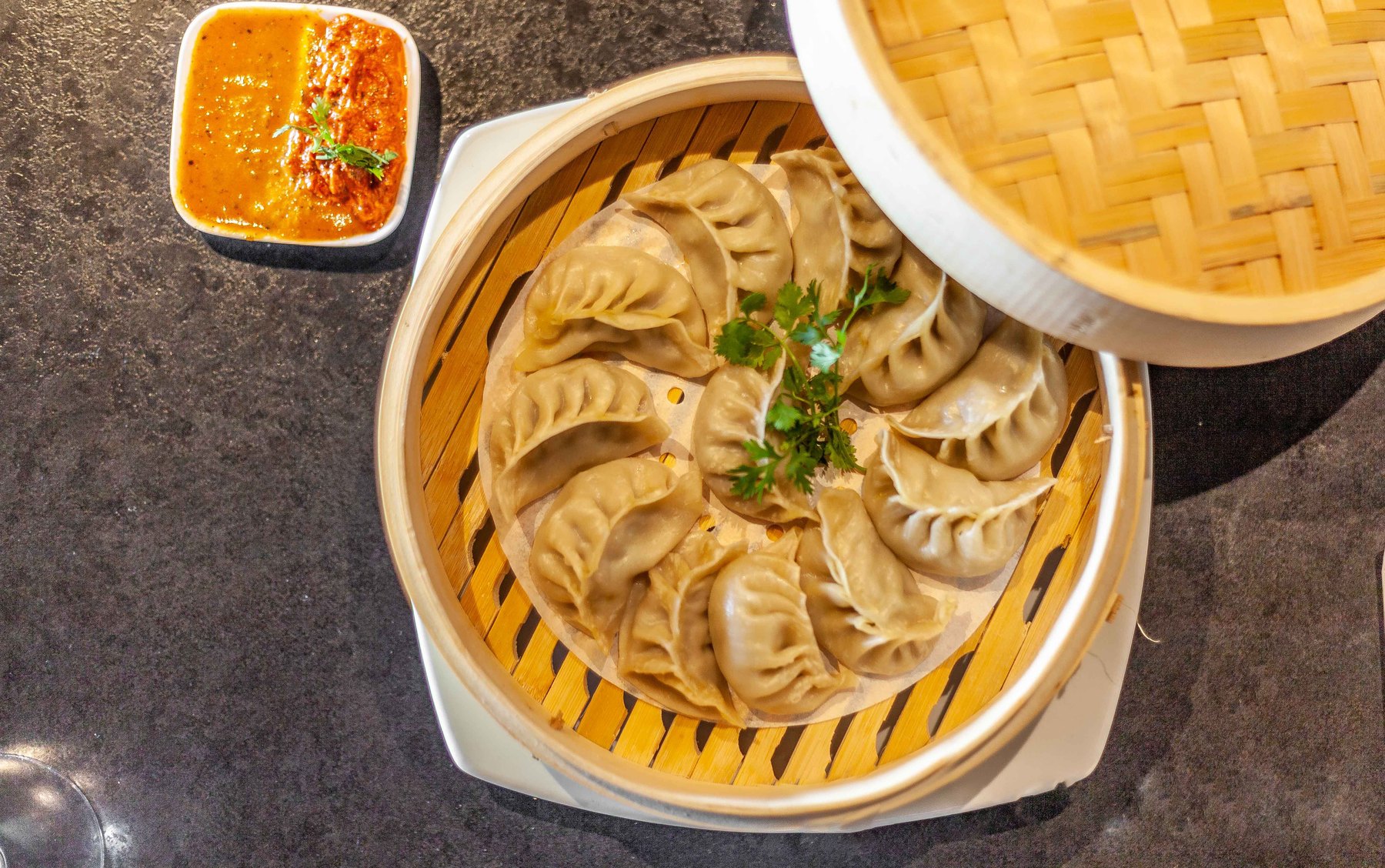 Steamed momos in a bamboo basket with house achar dips